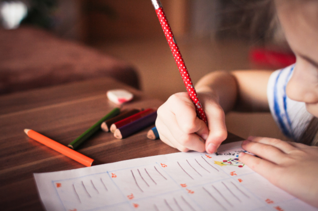 Closeup of a child's arms over a table as they draw on paper